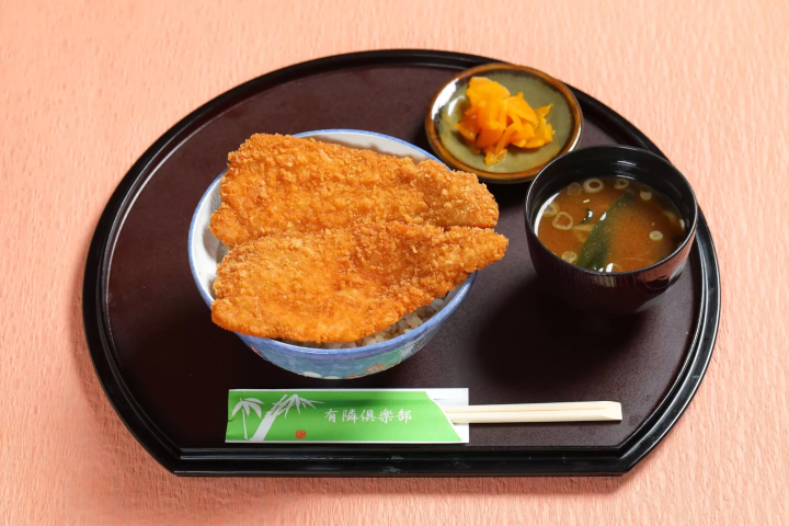 The cutlet is so big that it spills out of the bowl. 