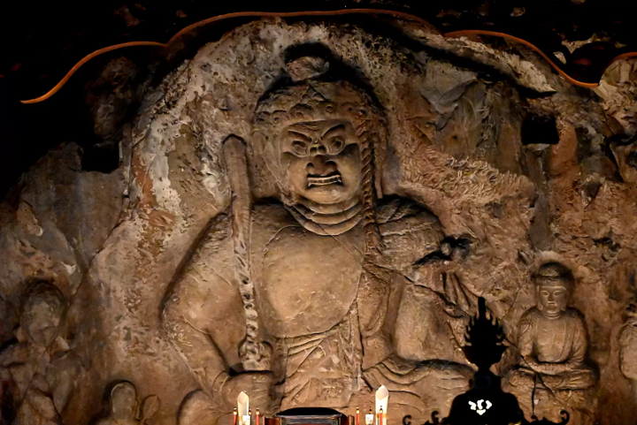 The impressive rock-carved Buddha statue of Acala is lit by a faint light in the dimly lit main hall. 